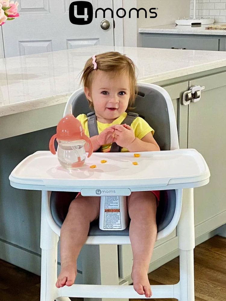 a toddler girl sitting in the 4moms high chair and eating food