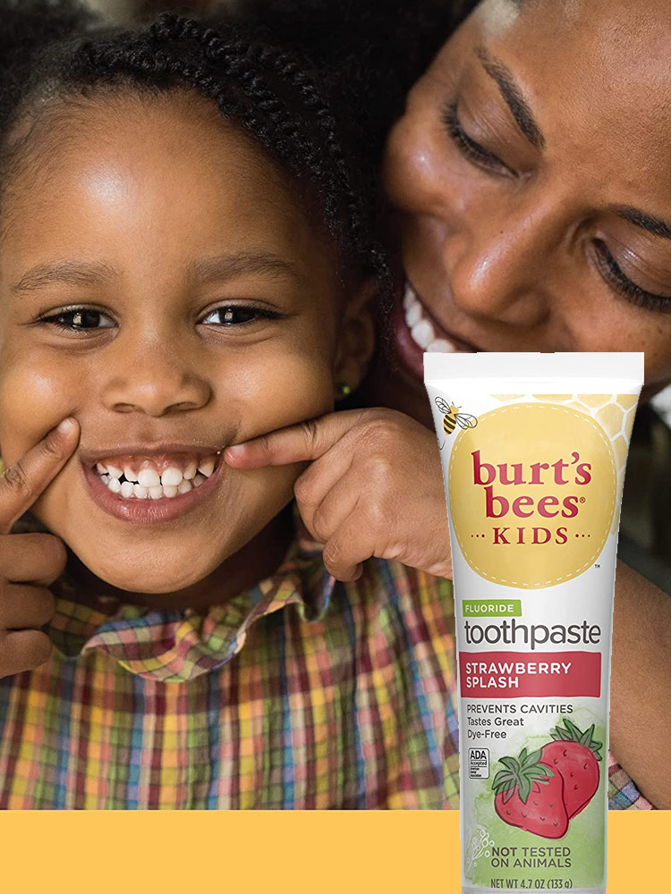 a toddler girl smiling and mom looking over her shoulder while using burts bees kids toothpaste
