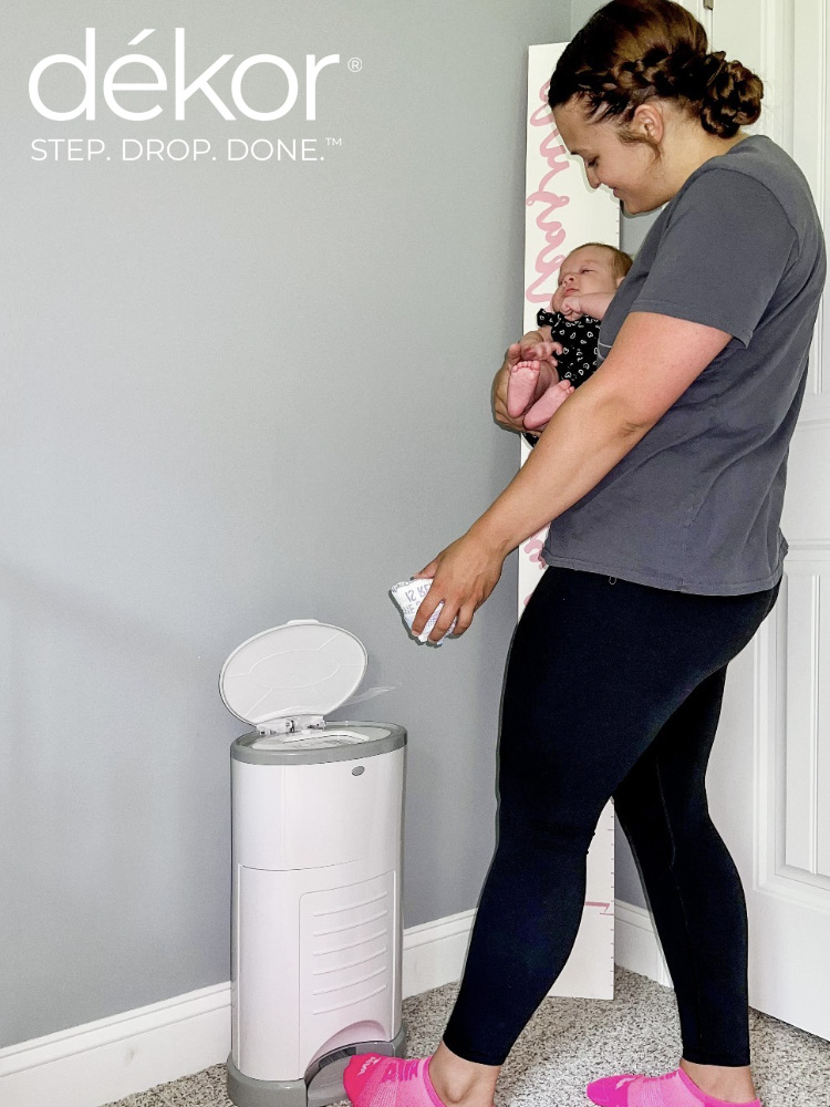 a mom holding a newborn baby and disposing a dirty diaper in the diaper dekor pail