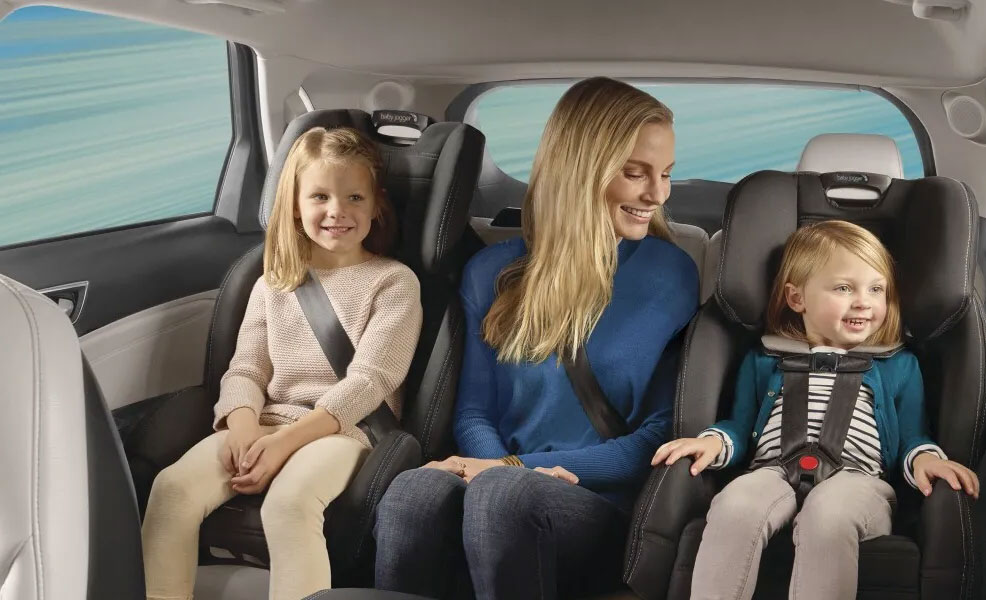 mom sitting in back seat with children riding in baby jogger city view car seats