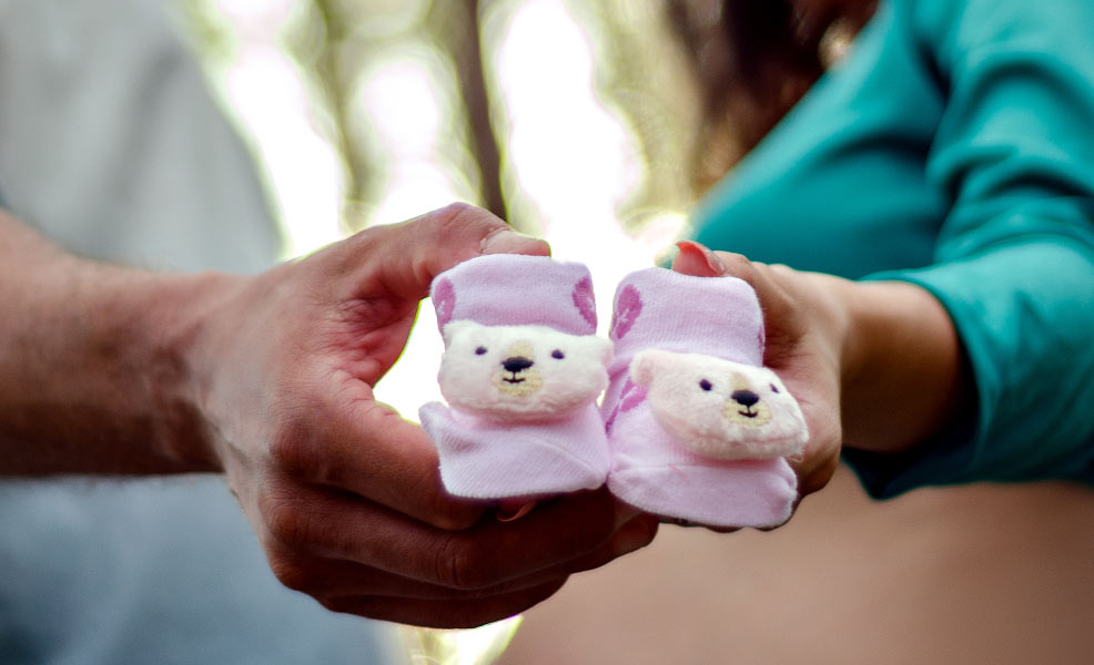 expectant parents holding pink baby shoes