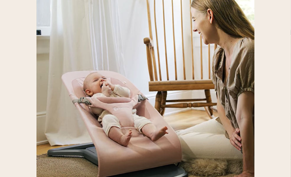 a mom smiling at her baby sitting in an ergobaby evolve bouncer seat
