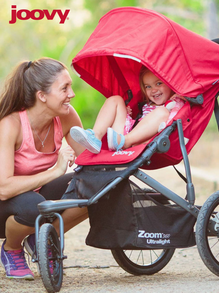 a woman looking at her smiling baby who is riding in the joovy zoom 360 stroller