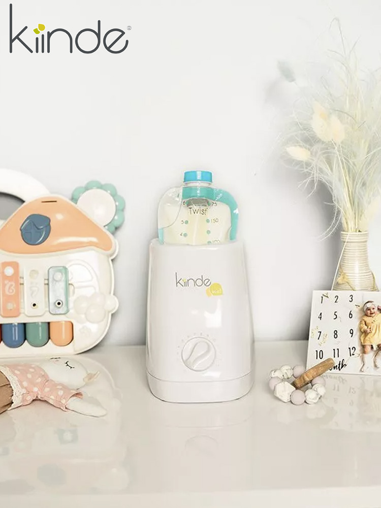 a pouch of breast milk getting warmed in the kiinde kozii bottle warmer next to toys
