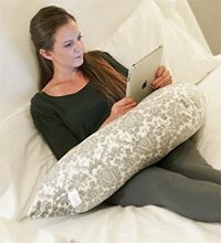 a woman laying in bed reading a book while laying on the Luna Lullaby Bosom Pillow
