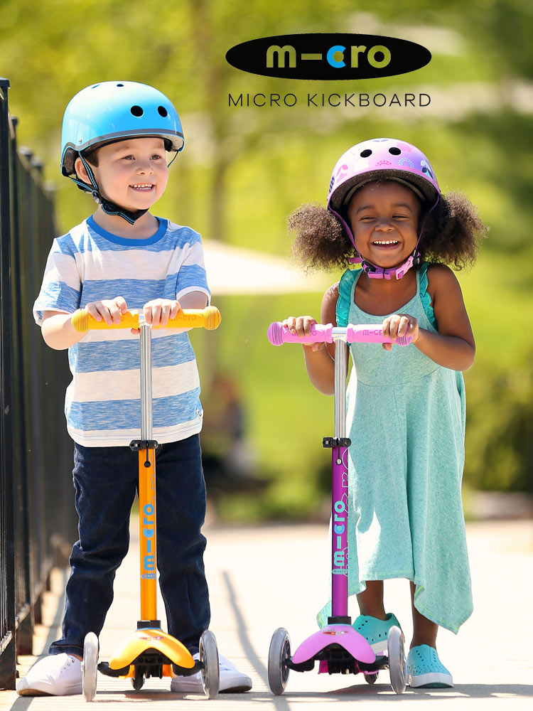 two young kids standing on micro mini deluxe scooters