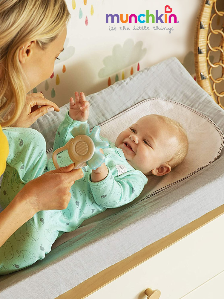 a mom entertaining a baby with a rattle during a diaper change on the munchkin secure grip changing pad