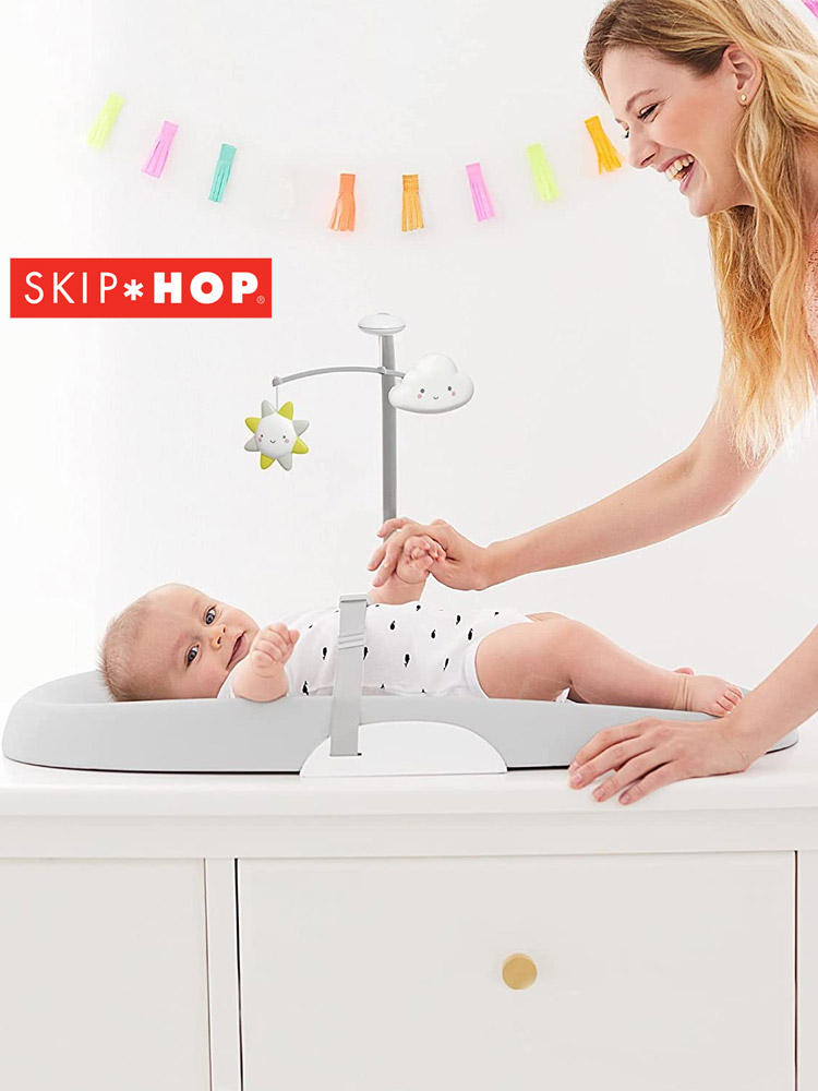 a mom holding a babys hand while doing a diaper change on the skip hop changing pad