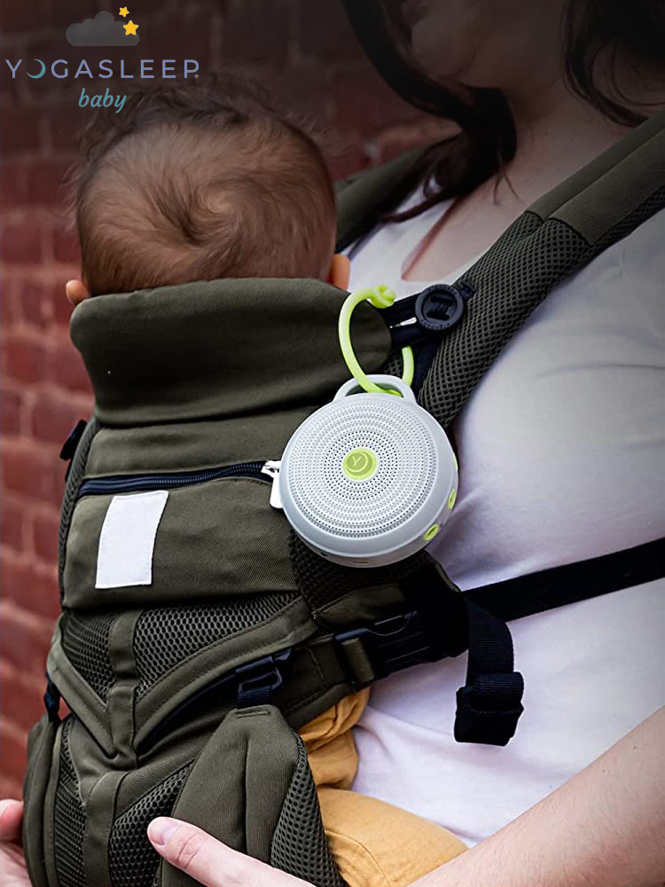 a mom with a baby in a baby carrier with the marpac yogasleep hushh sound machine hanging on a strap
