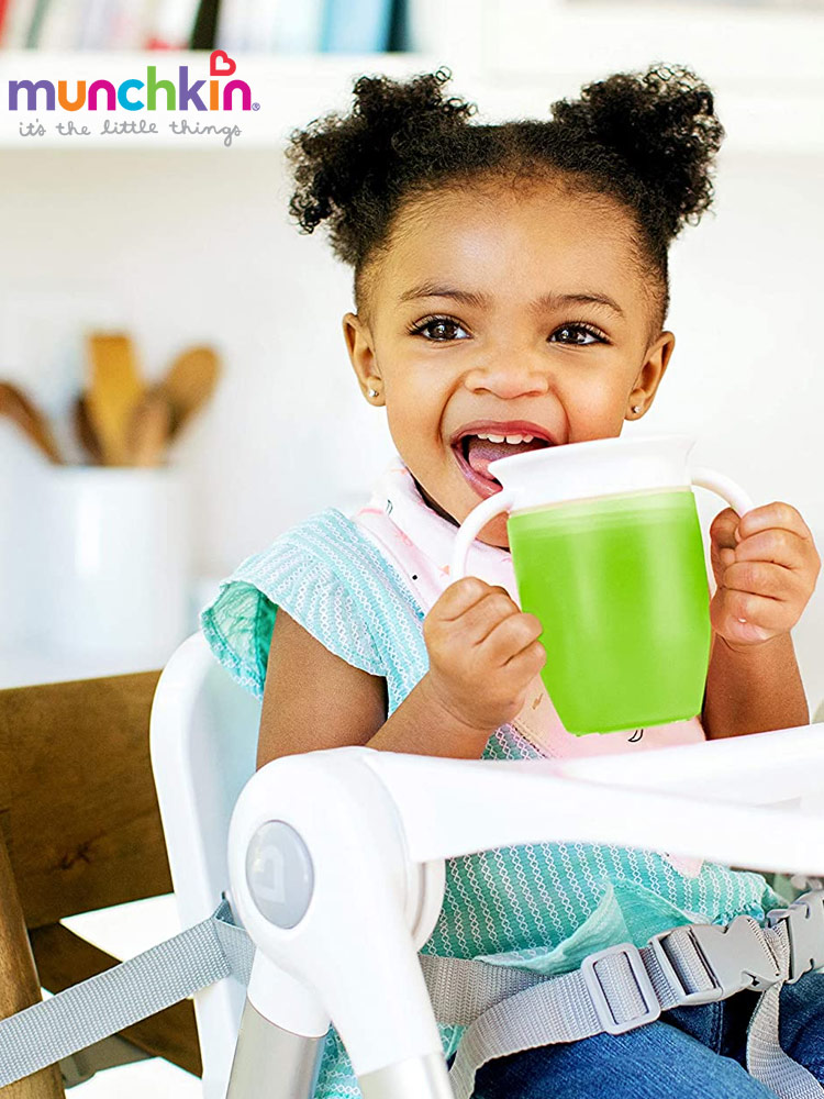 a toddler girl sitting in a high chair while drinking from the munchkin miracle 360 trainer cup