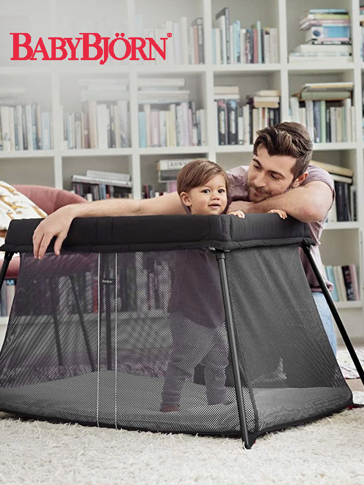 a father looking at a toddler standing in the babybjorn travel crib light