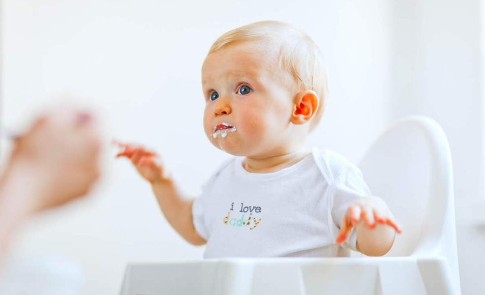 a baby sitting in a high chair being spoon-fed baby cereal