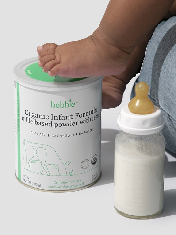 a tin of bobbie infant formula with a baby foot on top next to a bottle filled with formula