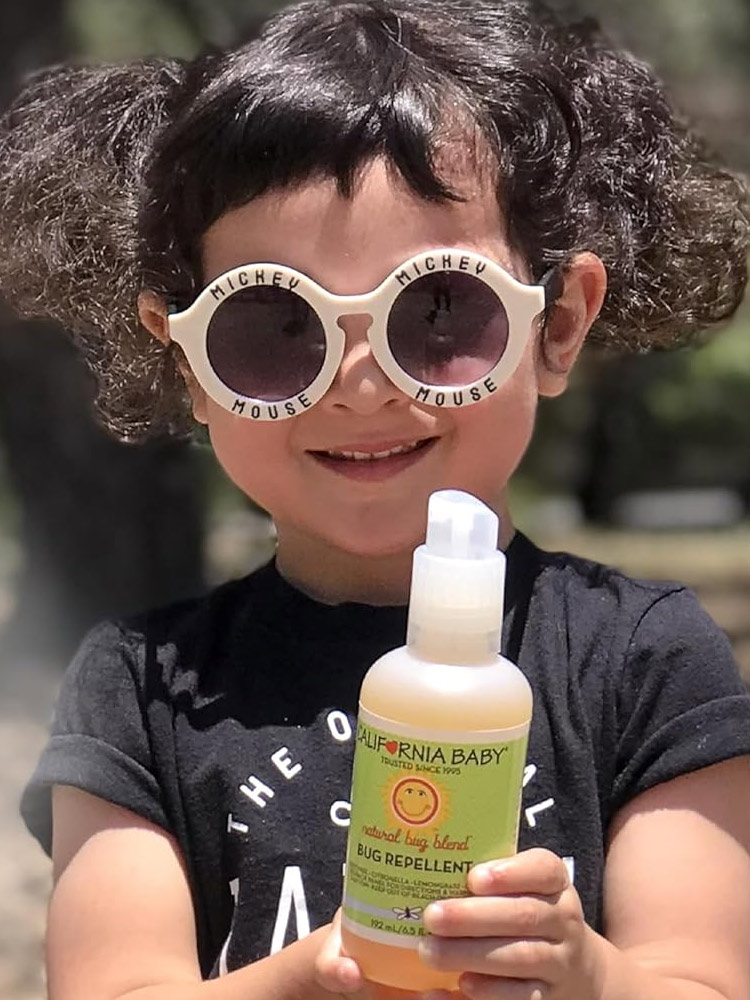 a child holding a spray bottle of California baby natural bug repellent