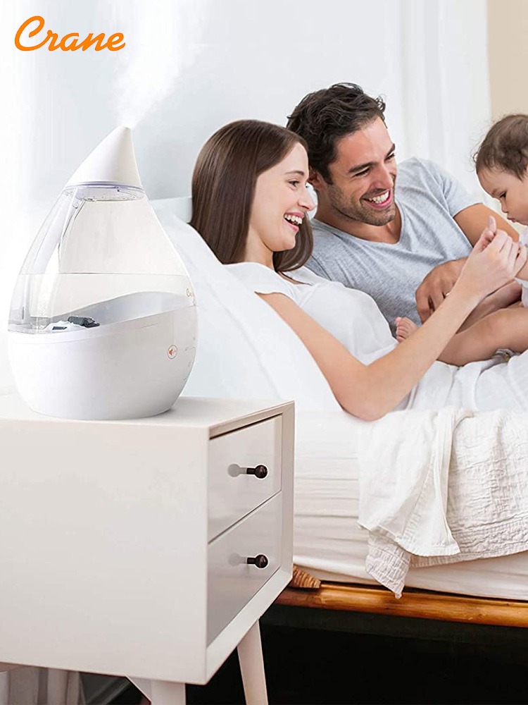 parents playing with baby in bed while crane drop humidifier is running
