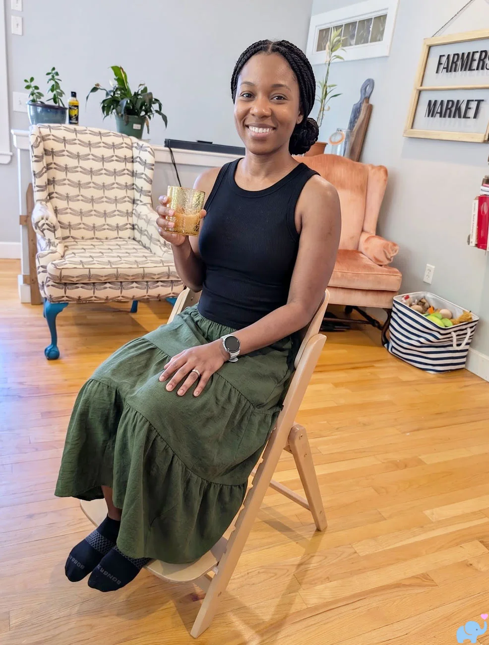 Adult woman sitting comfortably in the Delta Children Crave High Chair adult configuration while holding a glass of water