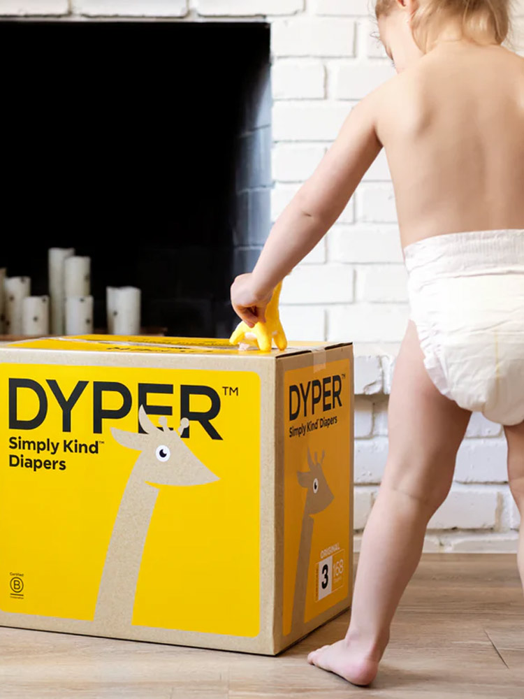 toddler standing next to a box of dyper diapers