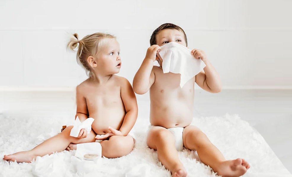 two toddlers playing with baby wipes while sitting on a rug