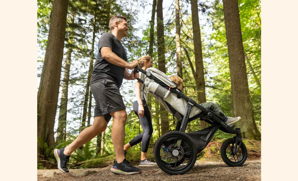 parents pushing all-terrain stroller while hiking in forest