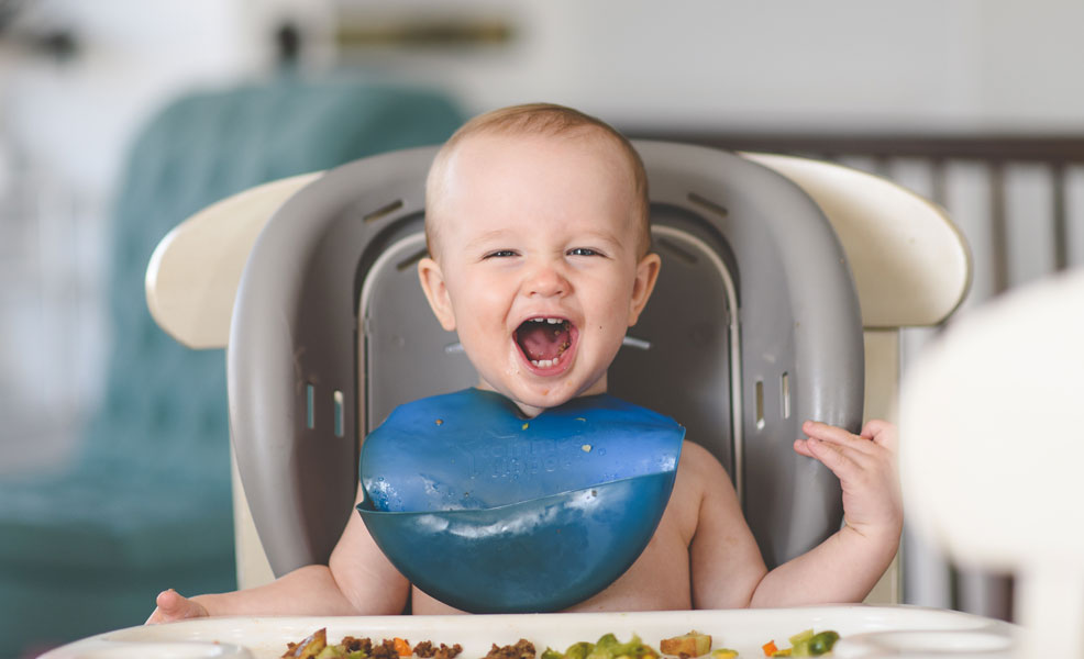 messy toddler eating food in a high chair