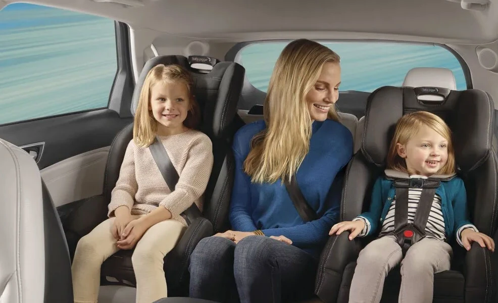 mom sitting in back seat with children riding in baby jogger city view car seats