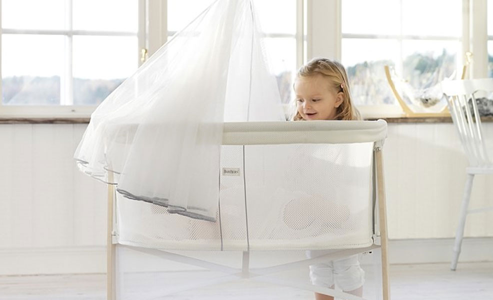 older sister peeking into the babybjorn cradle bassinet where a baby is sleeping