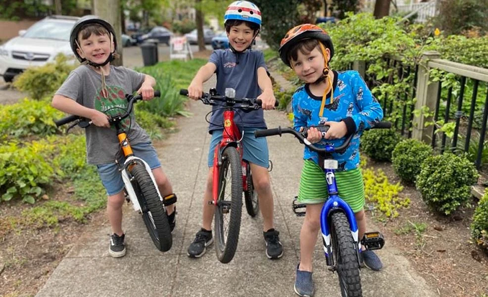 three kids standing with their bikes on the sidewalk