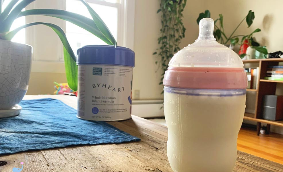 byheart baby formula on a table alongside a baby bottle filled with the formula