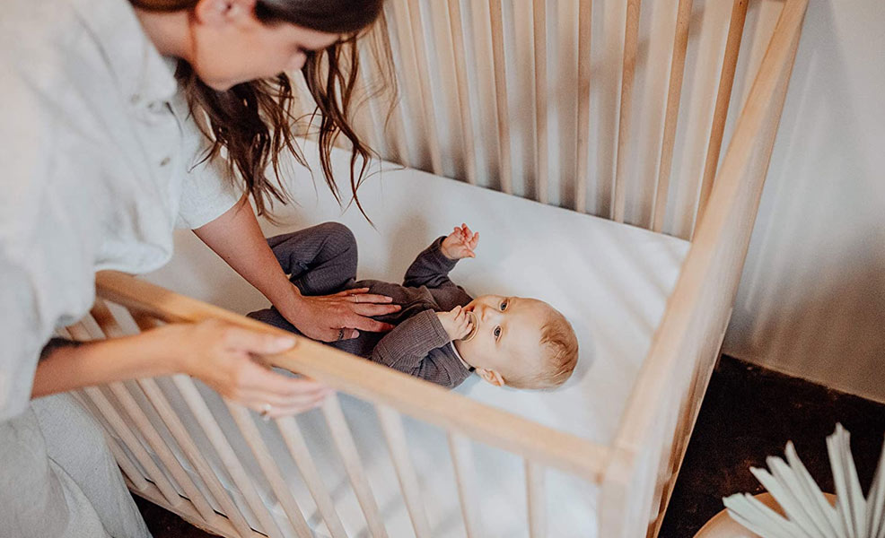 a mother putting a baby to sleep on the colgate ecoclassica iii crib mattress