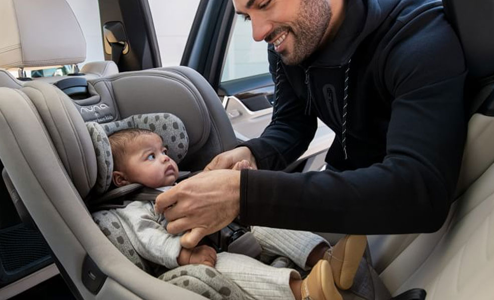 man buckling the harness of nuna rava convertible car seat with a baby in the seat