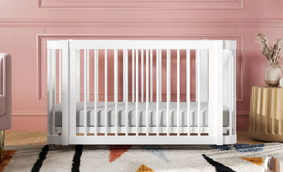 a white nestig crib in a nursery with red walls and a rug