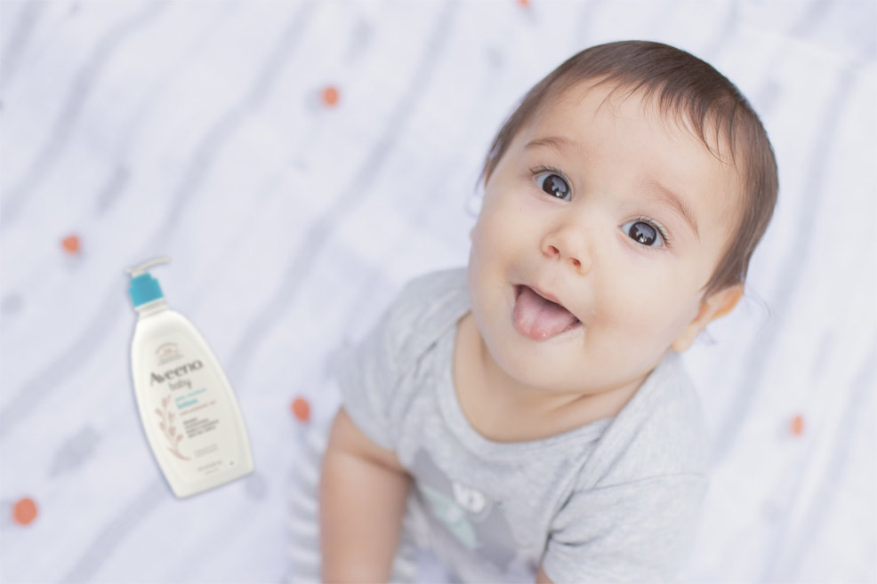 baby sitting on a bed next to a tube of baby lotion