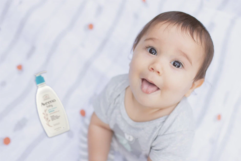 baby sitting on a bed next to a tube of baby lotion