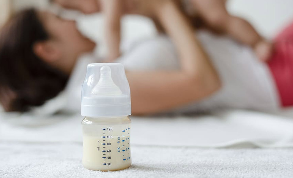 a glass baby bottle with mom and baby in background