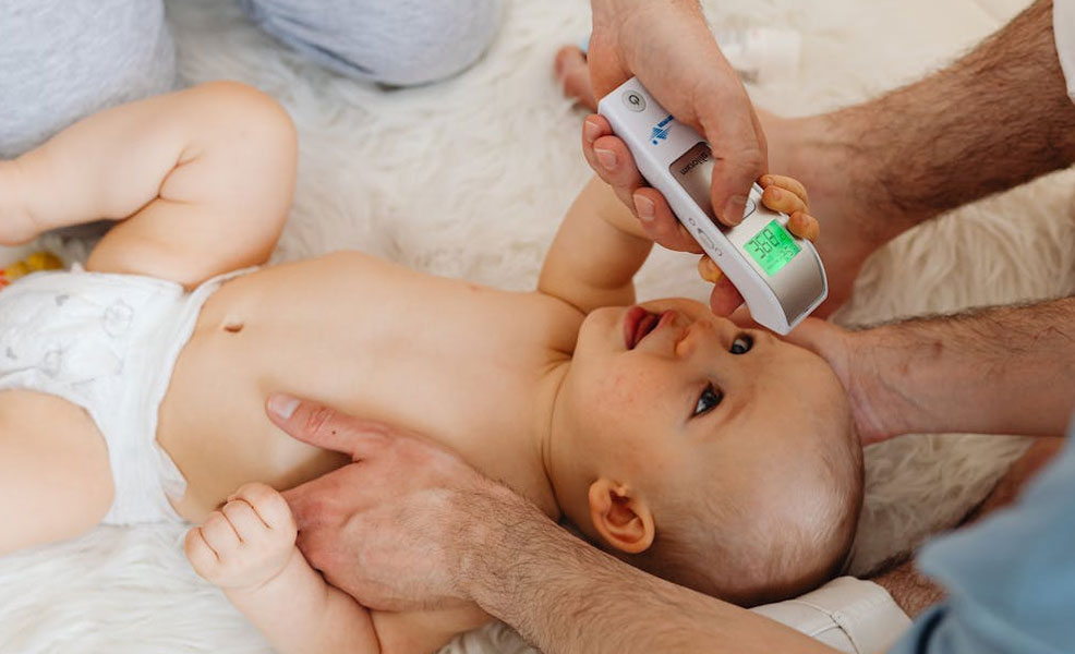 parents using a baby thermometer to scan the forehead of an infant