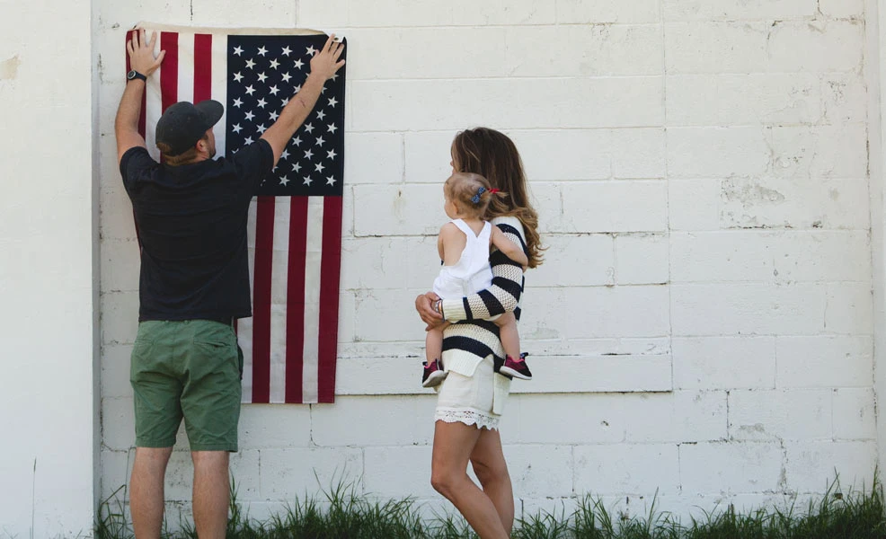 parents holding a baby and hanging an american flag