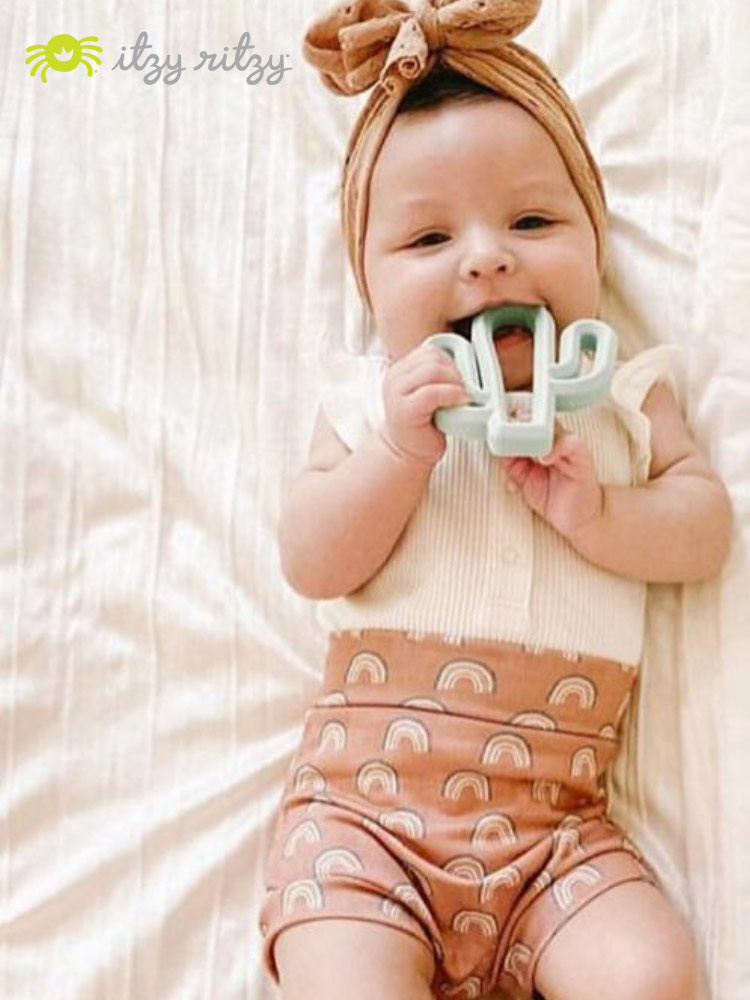 a happy baby laying down and chewing on an itzy ritzy teething toy