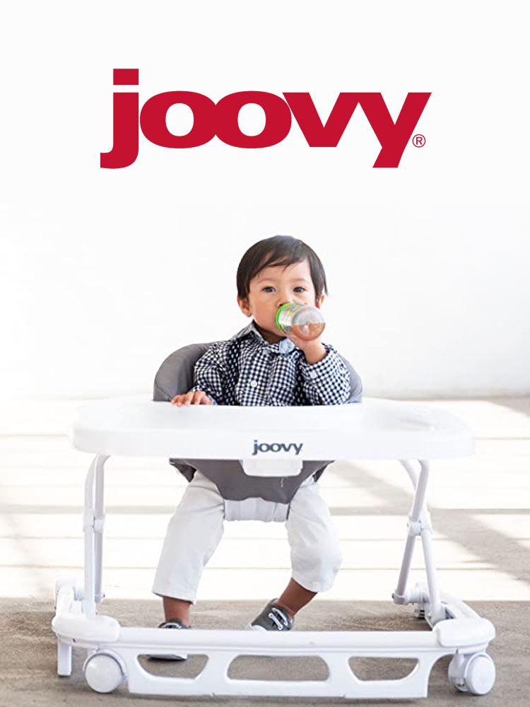 a toddler boy drinking from a bottle while sitting in the joovy spoon baby walker