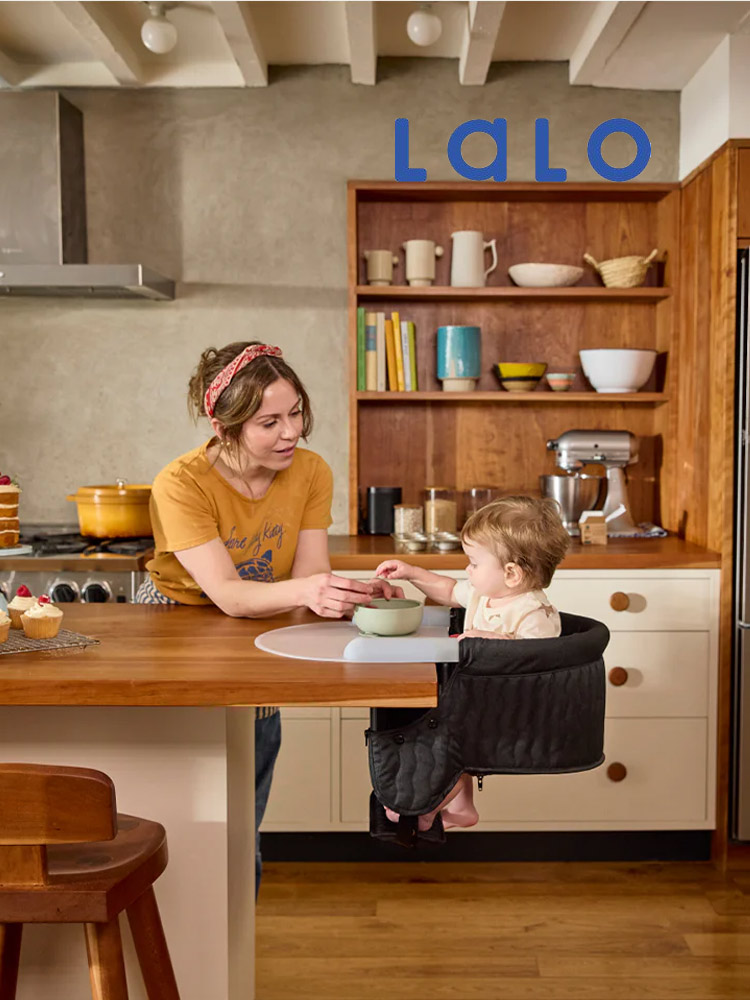 a toddler sitting in the Lalo Hook-on high chair and eating food