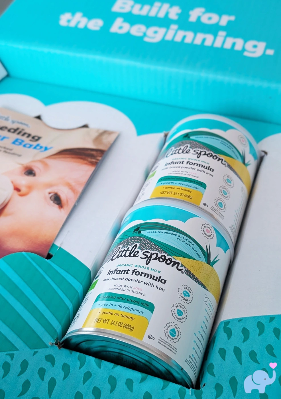 the Little Spoon formula unboxing showing the opened shipping box with two tins of formula inside and a bottle-feeding instruction booklet