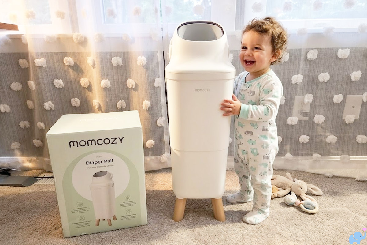 momcozy diaper pail being reviewed in a nursery with a toddler standing next to it