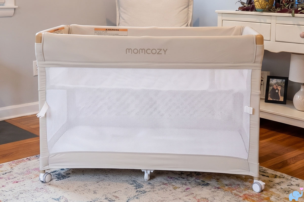 the momcozy one-click foldable playard and bassinet in a living room background