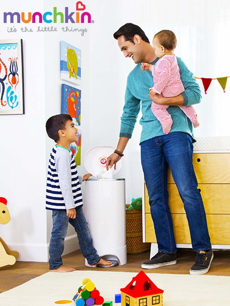 a dad holding a baby while disposing of a dirty diaper in the munchkin step diaper pail