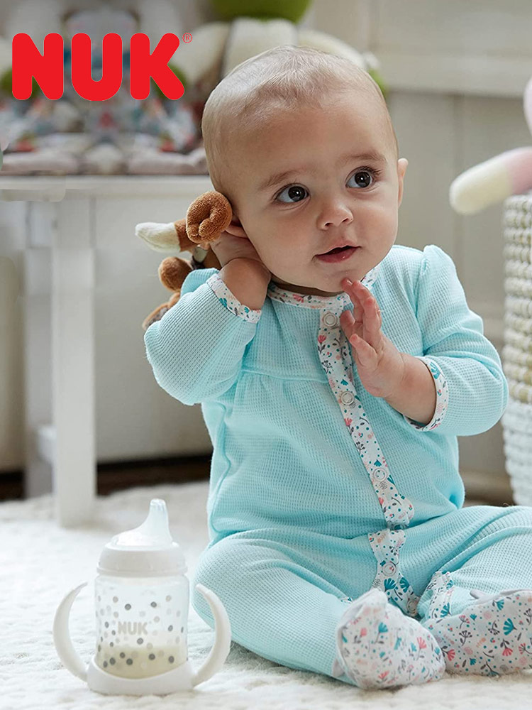 a baby sitting and playing next to a nuk learner sippy cup