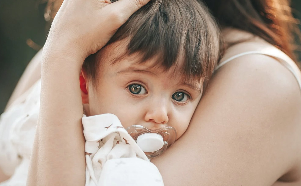 baby boy being held by mom with a pacifier in mouth