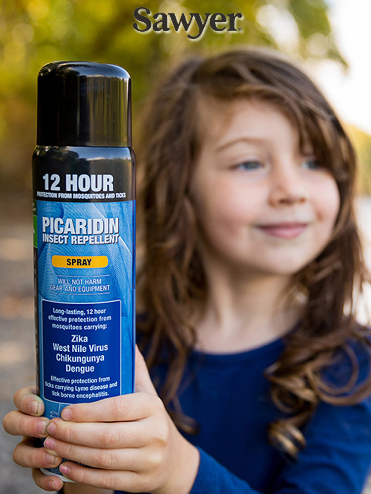 a girl in the woods holding a bottle of sawyer premium bug spray