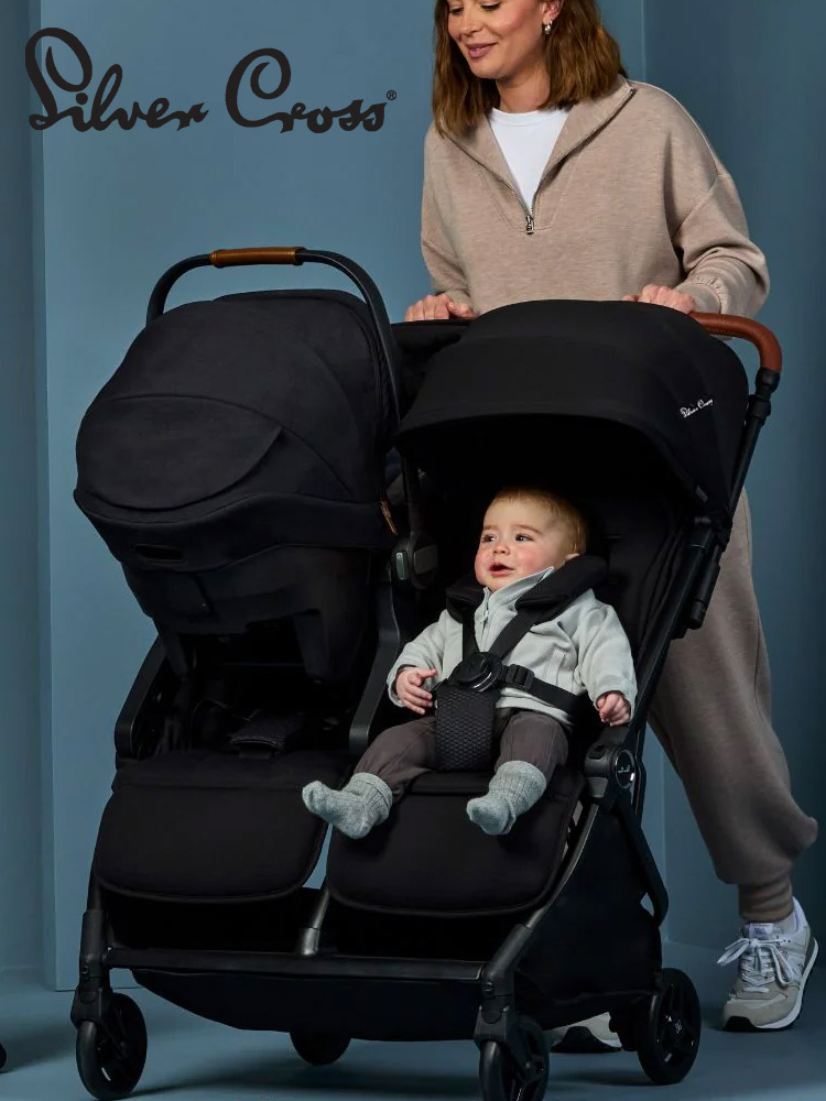 a mom pushing the silver cross jet double stroller with a toddler in one seat and an infant car seat attached