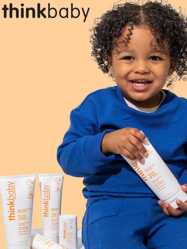 toddler boy sitting with a tubes of thinkbaby sunscreen