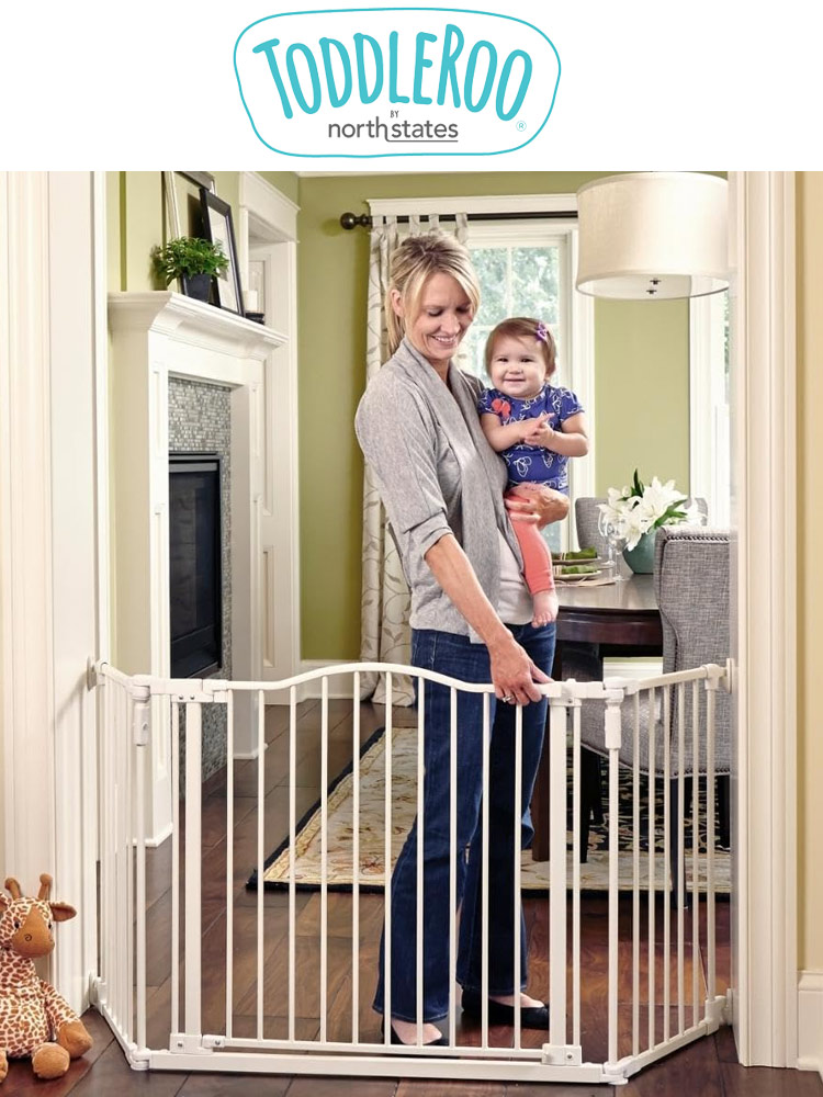 a mother carrying a baby and opening the north states toddleroo deluxe decor baby gate
