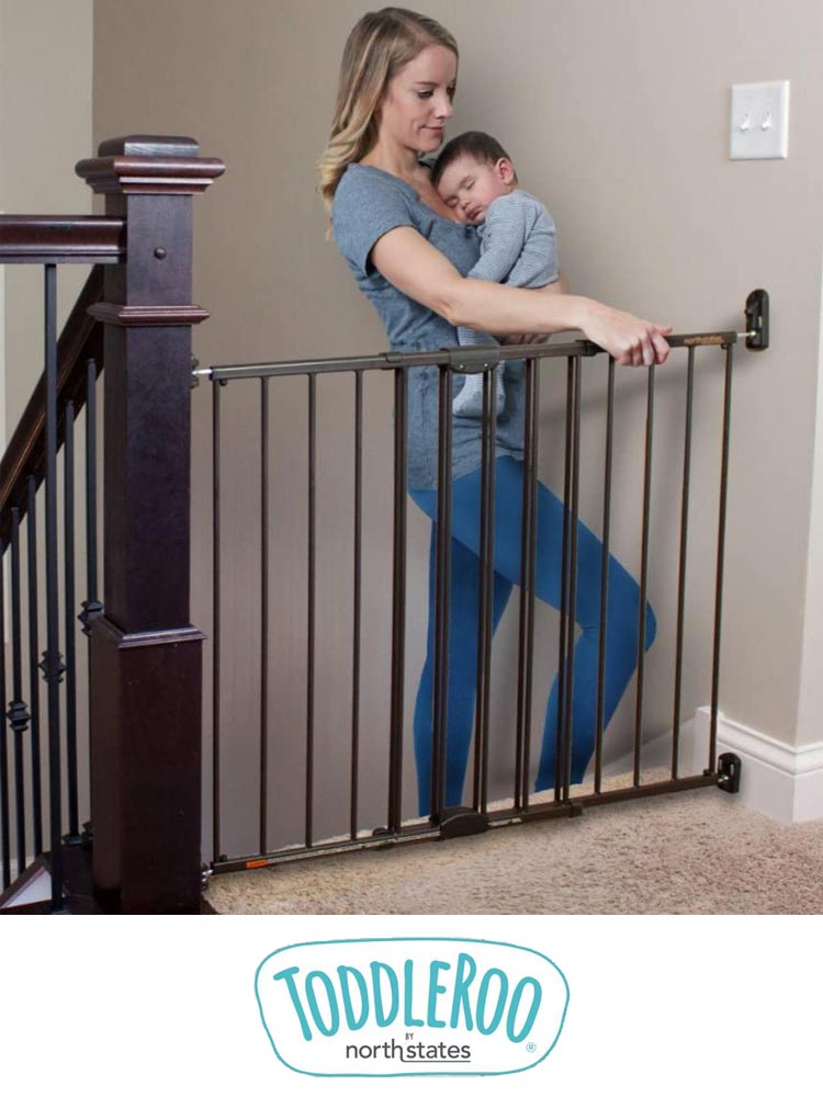 a mom holding a baby walking up the stairs and opening the toddleroo gate